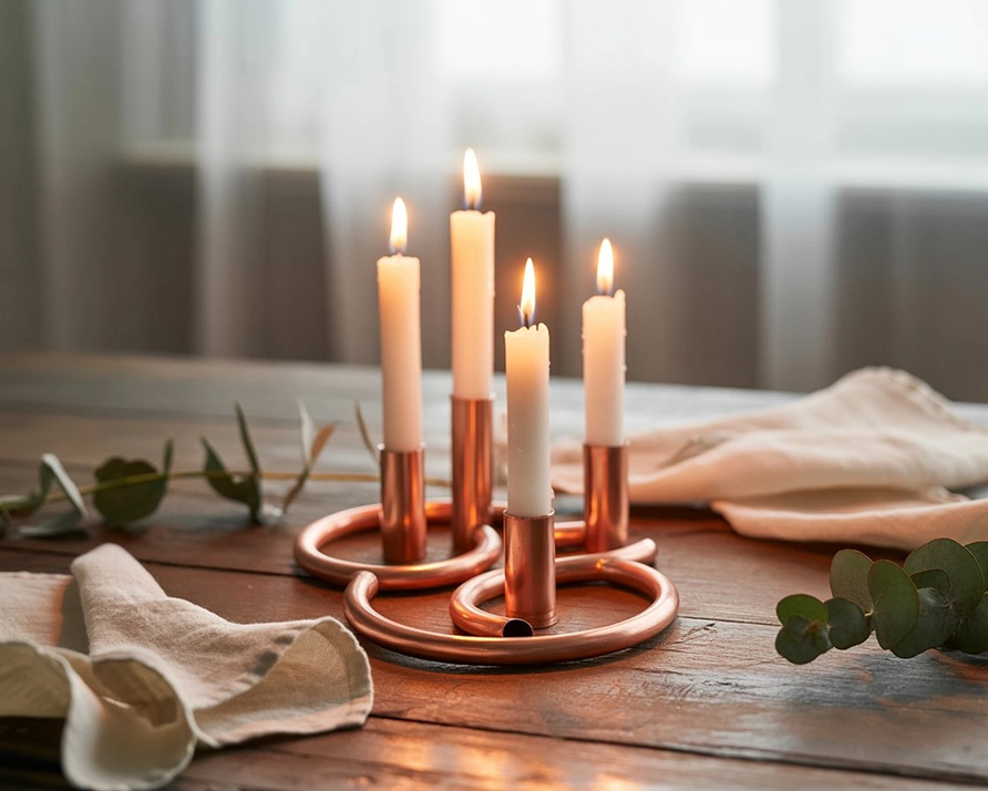 Handmade copper pipe candle holders with lit taper candles on a rustic table, surrounded by eucalyptus and soft linens.
